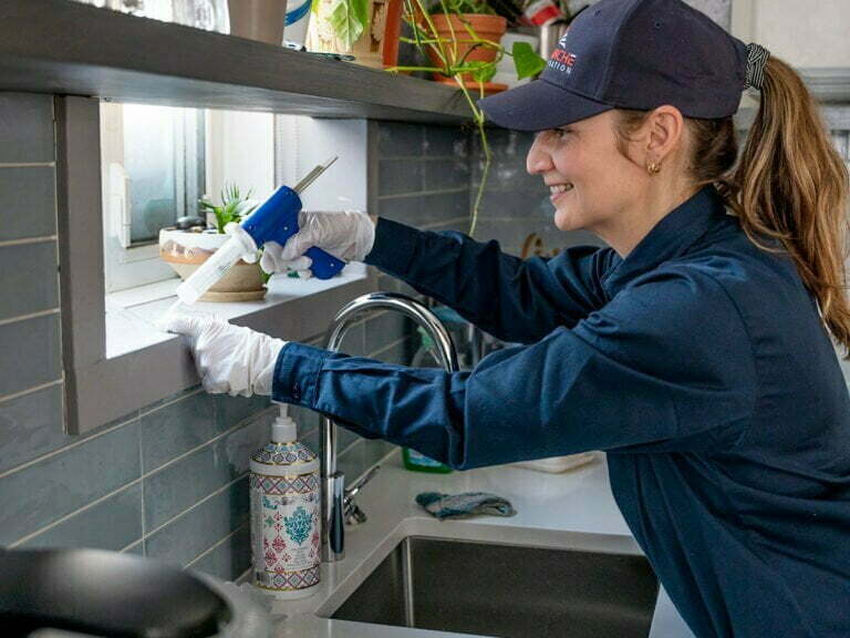 Technicienne applicant un produit contre les fourmis a l'interieur d'une fenetre